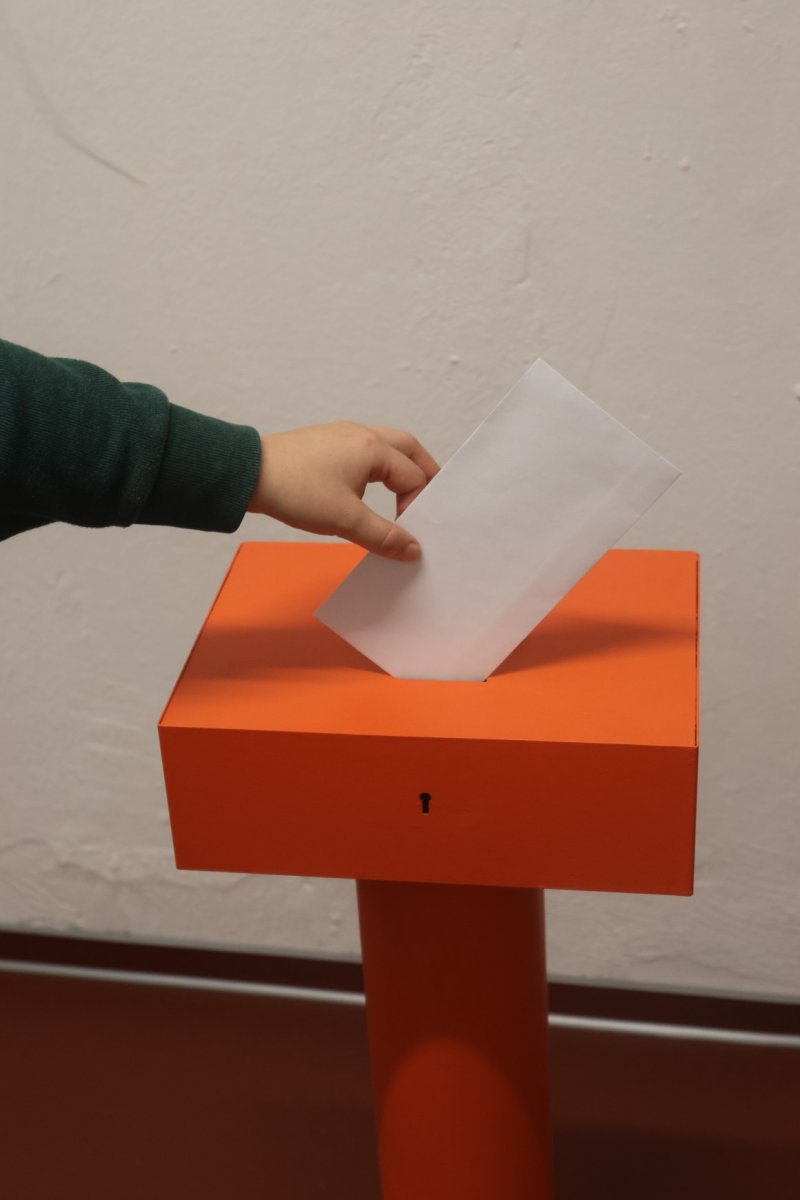 Bild einer Hand, die einen Abstimm-Zettel in einen Briefkasten würft.